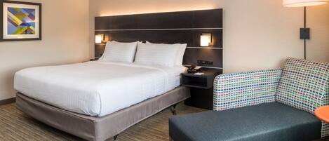 A hotel room with a bed, a nightstand, a lamp, and a patterned chair.