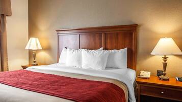 Une chambre d’hôtel avec une tête de lit en bois, une couvre-lit rouge, deux lampes de chevet et une table de chevet avec un téléphone et une horloge numérique.
