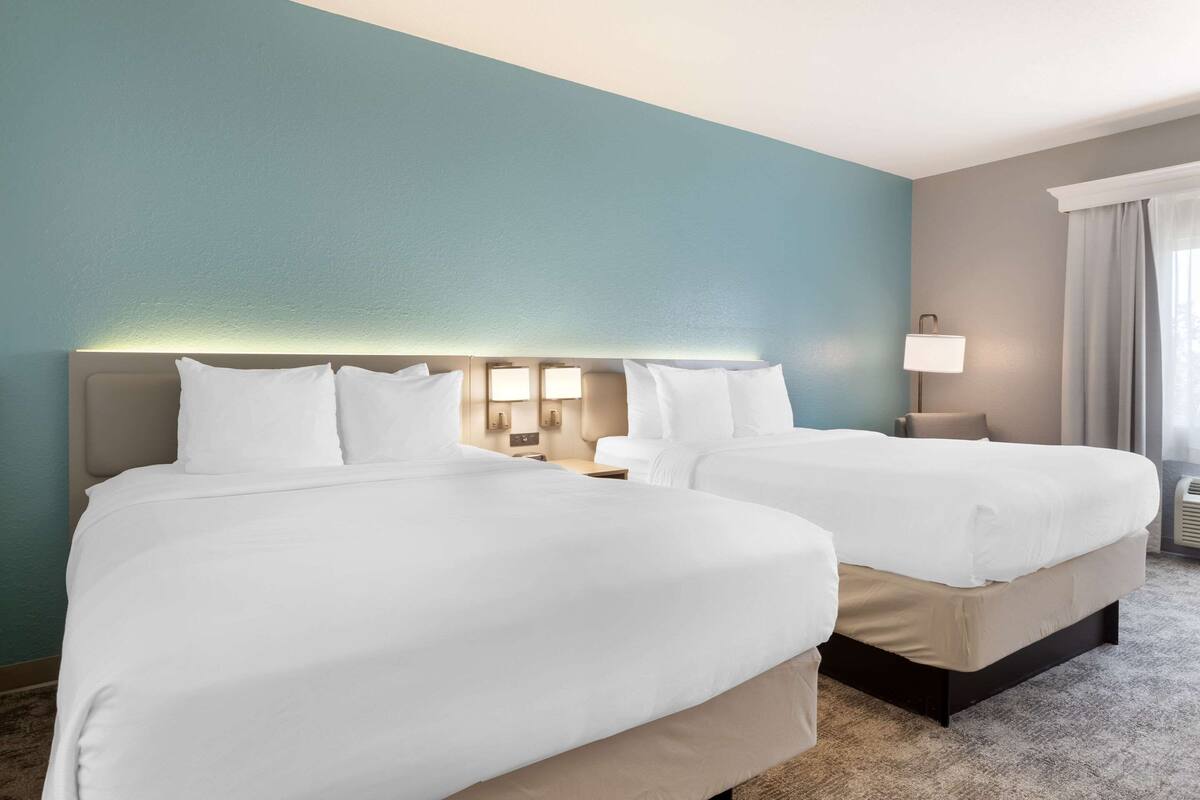 Una habitación de hotel con dos camas, una mesita de noche con lámpara y una ventana con cortinas.
