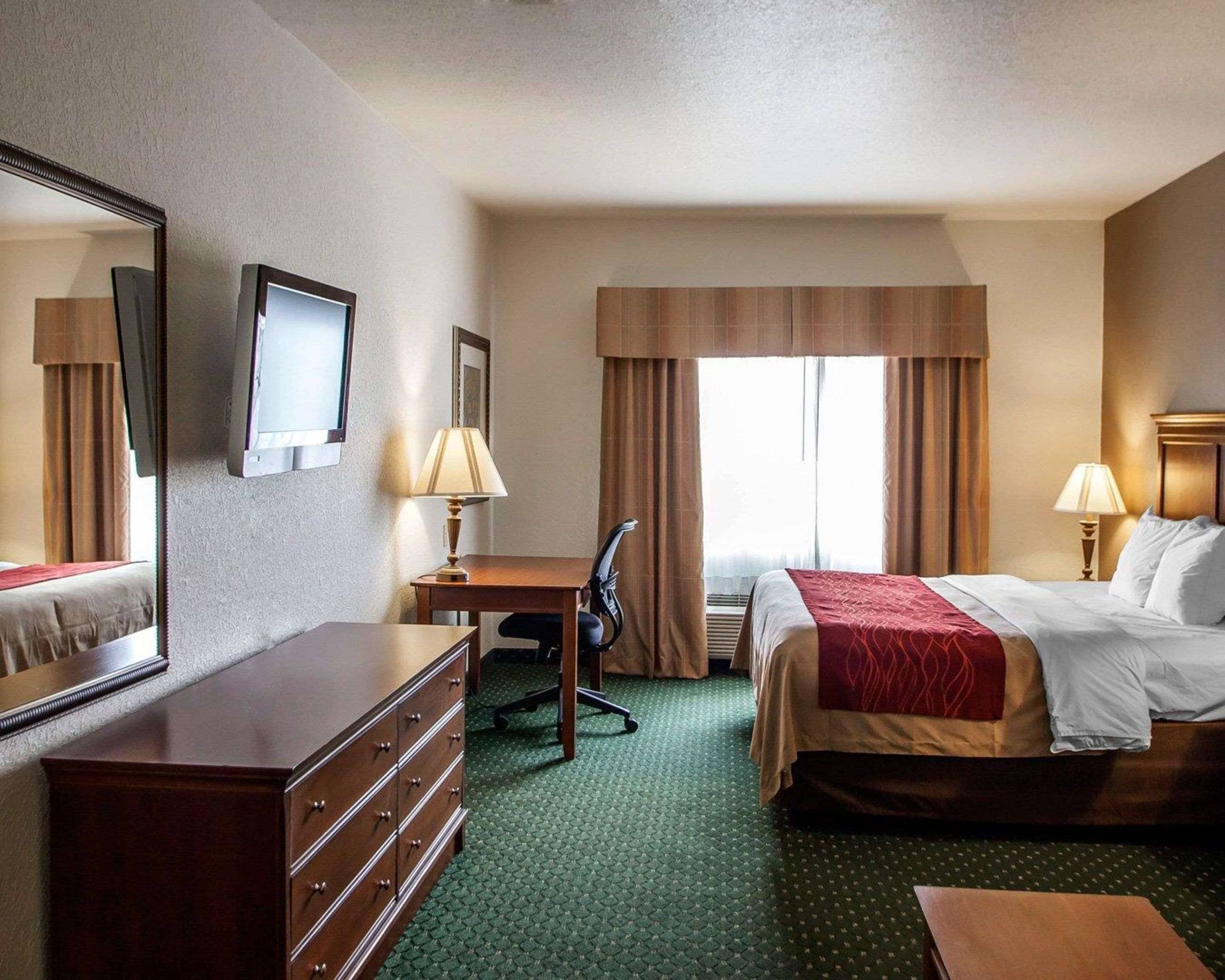 A hotel room with a bed, a desk, a chair, a dresser, and a large mirror.