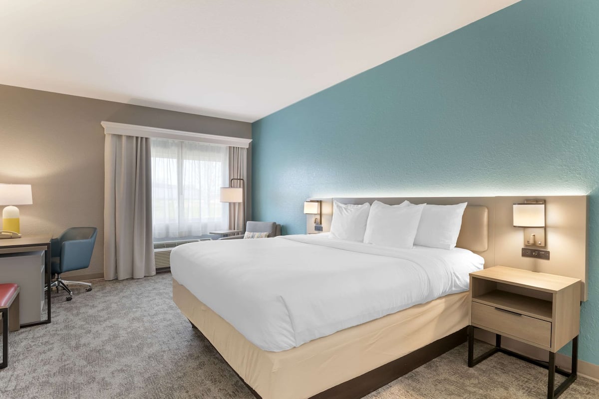 Una habitación de hotel con una cama grande, un escritorio con silla, una mesita de noche y una lámpara.