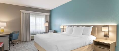 A hotel room with a large bed, a desk with a chair, a nightstand, and a lamp.