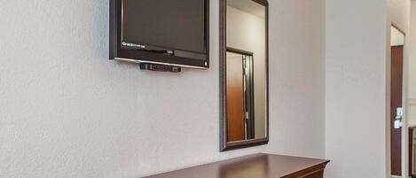 A hotel room with a wooden dresser, a flat-screen TV mounted on the wall, and a mirror above it.