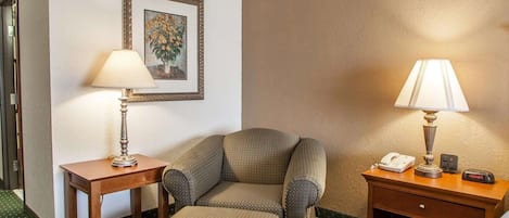 Habitación de hotel con sofá, una mesita con lámpara, un cuadro enmarcado en la pared y una mesita de noche con teléfono y reloj.