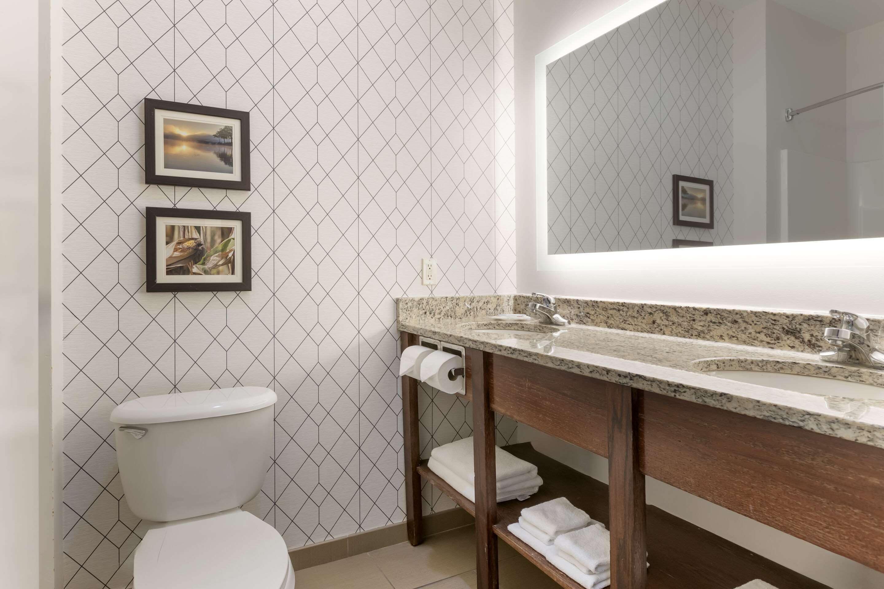 A modern bathroom with a toilet, a sink with a mirror, and two framed pictures on the wall.