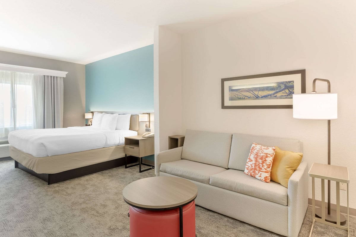 Una habitación de hotel con cama, sofá, una mesita y una lámpara.