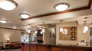 Un hall d’accueil d’hôtel avec un comptoir de réception en bois, plusieurs luminaires suspendus et une enseigne indiquant « Comfort Inn & Suites ».