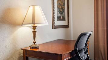 A wooden desk with a lamp, a black office chair, and a framed painting on the wall.
