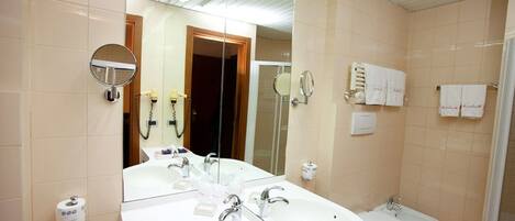 Un baño con un espejo grande, dos lavamanos, un inodoro y una zona de ducha.
