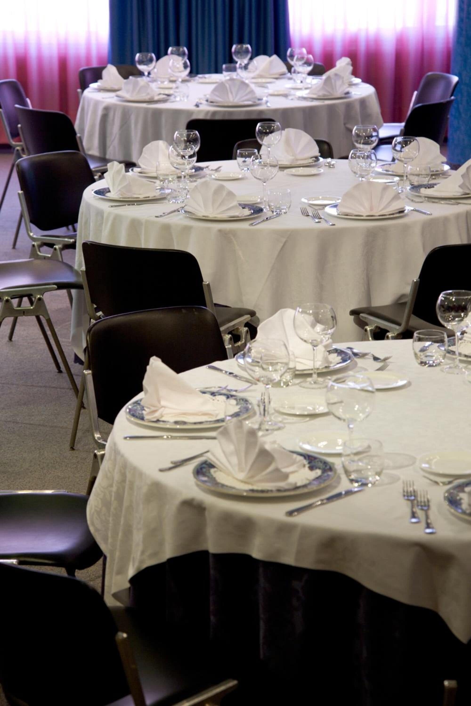 A dining area with round tables set for multiple guests, each with white tablecloths and blue and white plates.