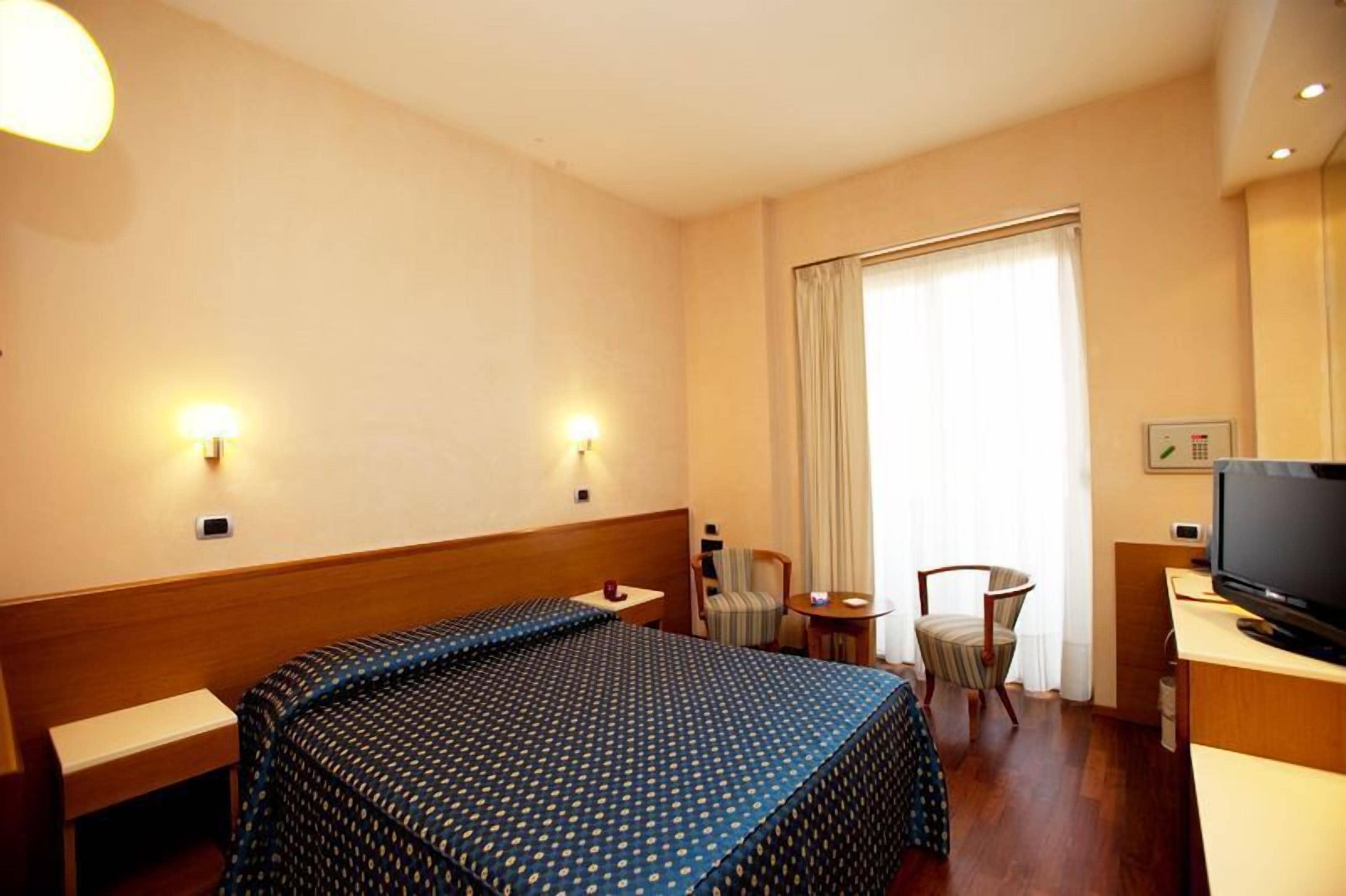 A hotel room with a bed, a desk, a chair, a television, and a window with curtains.