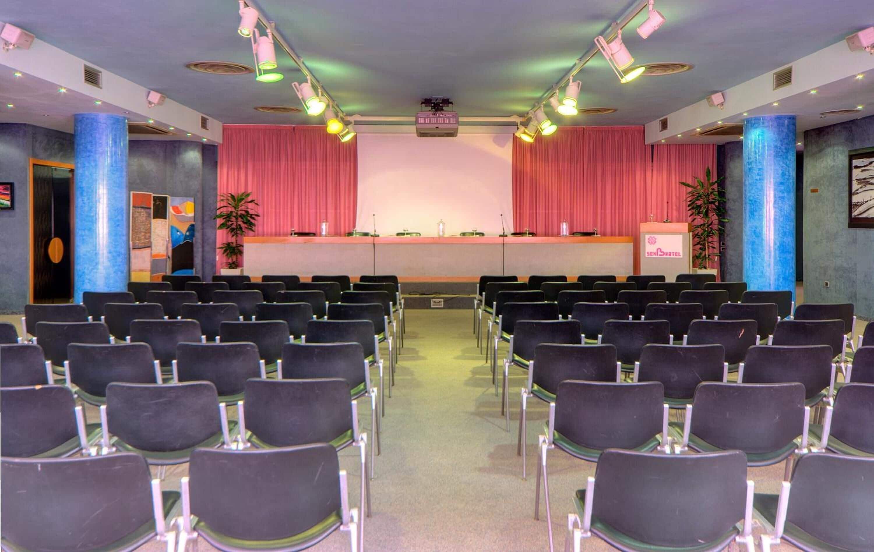 A conference room with rows of chairs, a podium, and a stage with curtains.