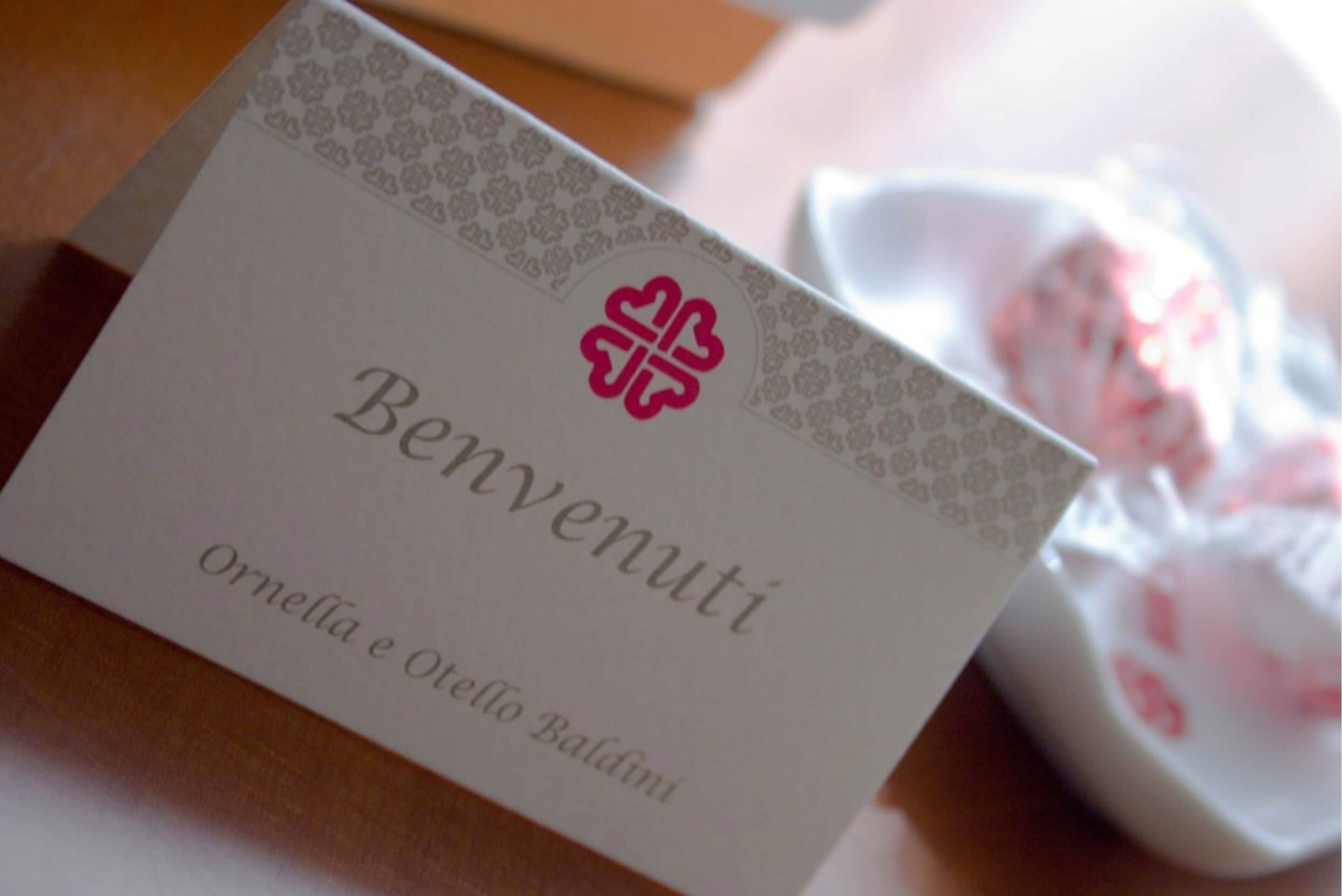 Una targeta blanca amb la inscripció "Benvenuti" i "Ornella e Oresto Baldini".
