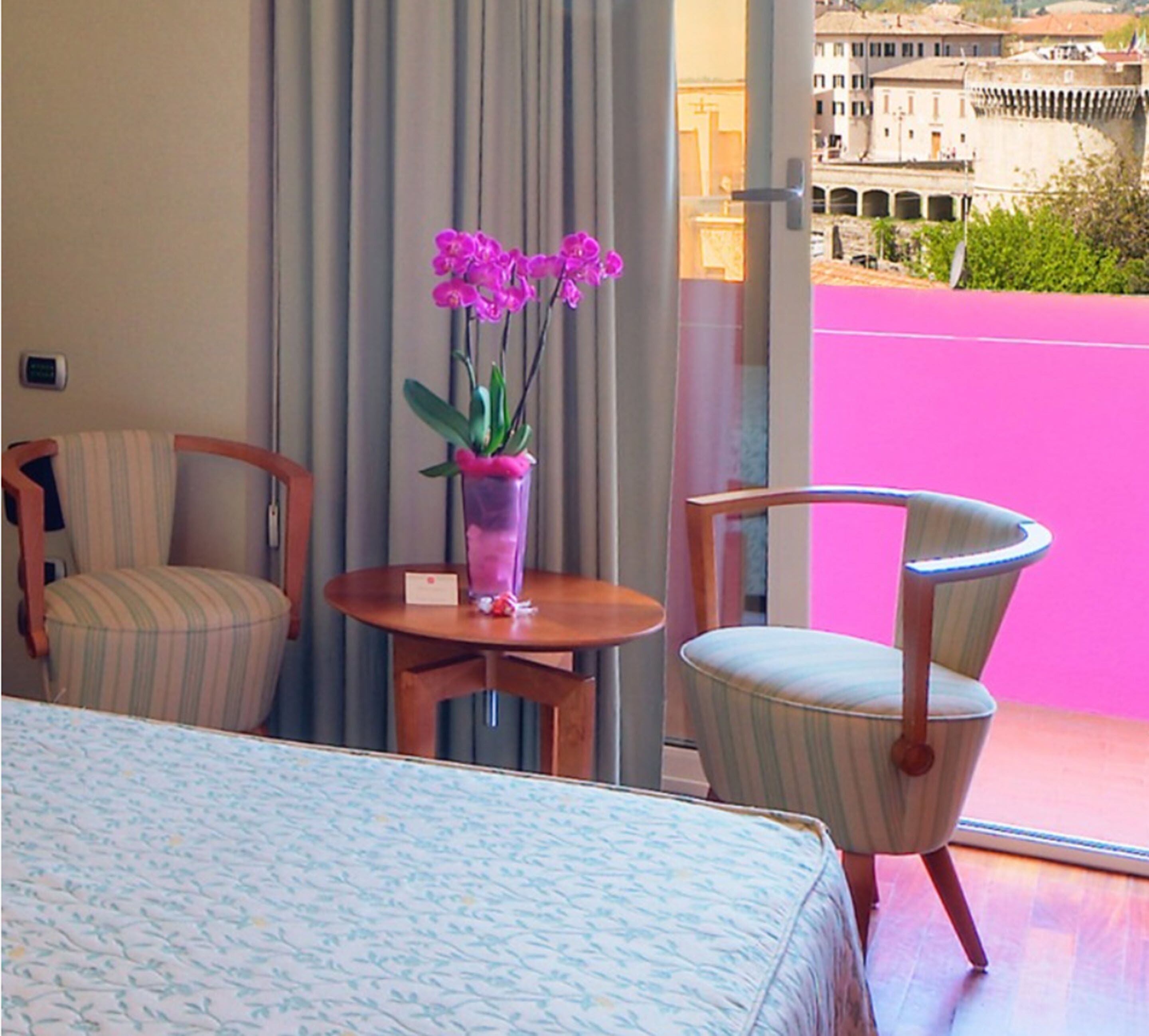 Ein Hotelzimmer mit einem Bett, zwei Stühlen, einem kleinen Tisch und einer Blumenvase.