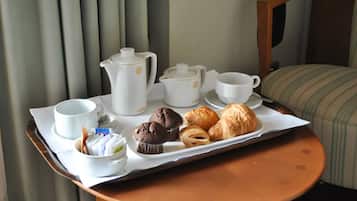 Ein Tablett mit einer Kaffeekanne, Tassen, einem Muffin und Croissants auf einem Tisch.