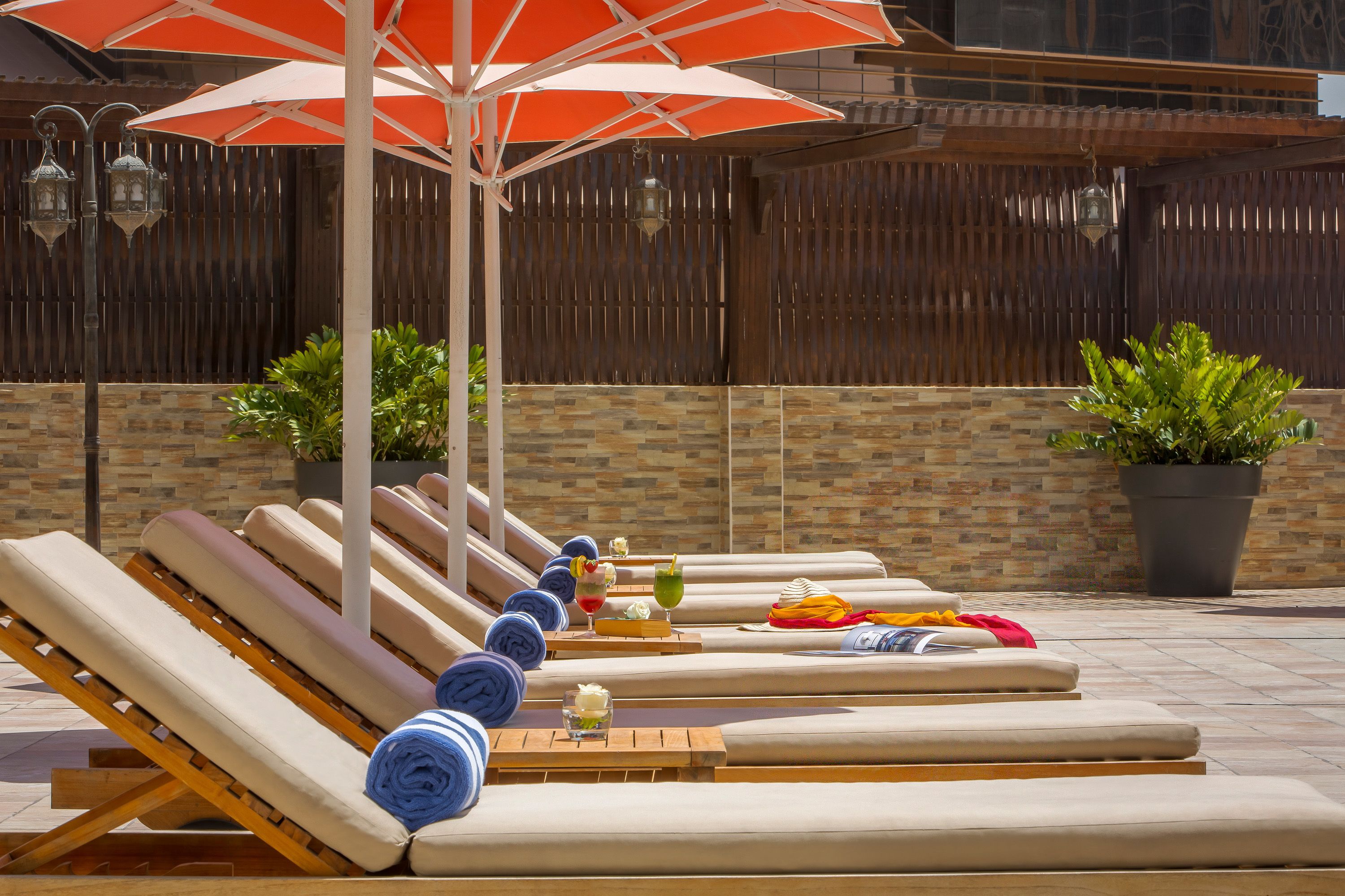 A sunlit outdoor lounge area with multiple lounge chairs and a large umbrella providing shade.