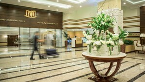 Eine Hotelhalle mit einer Rezeption, einer großen dekorativen Vase mit Blumen und einem Schild für Konferenzräume.