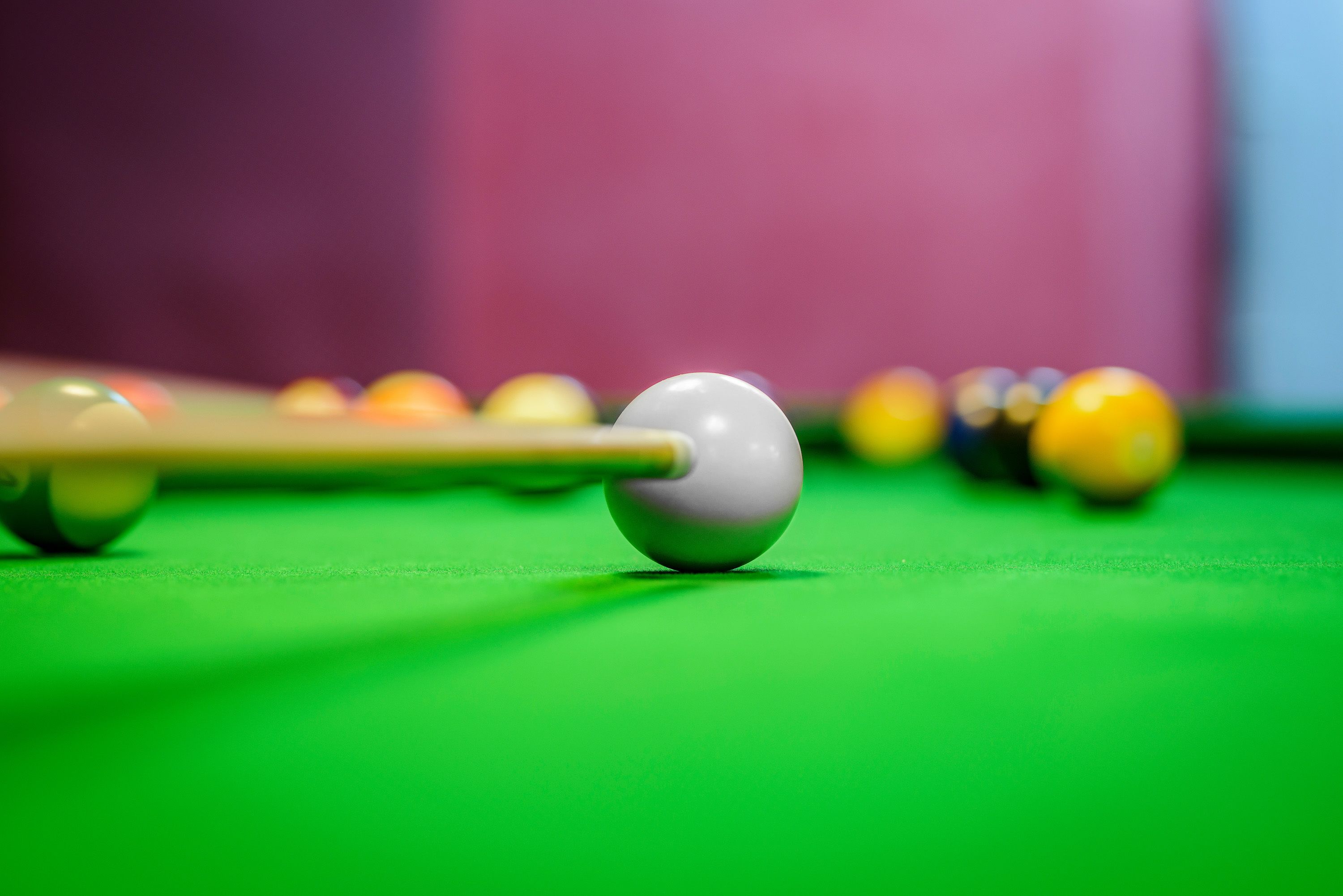 A close-up of a billiards cue striking a white cue ball on a green felt table.