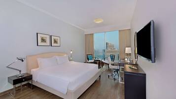 A hotel room with a bed, desk, chair, TV, and a window with a city view.