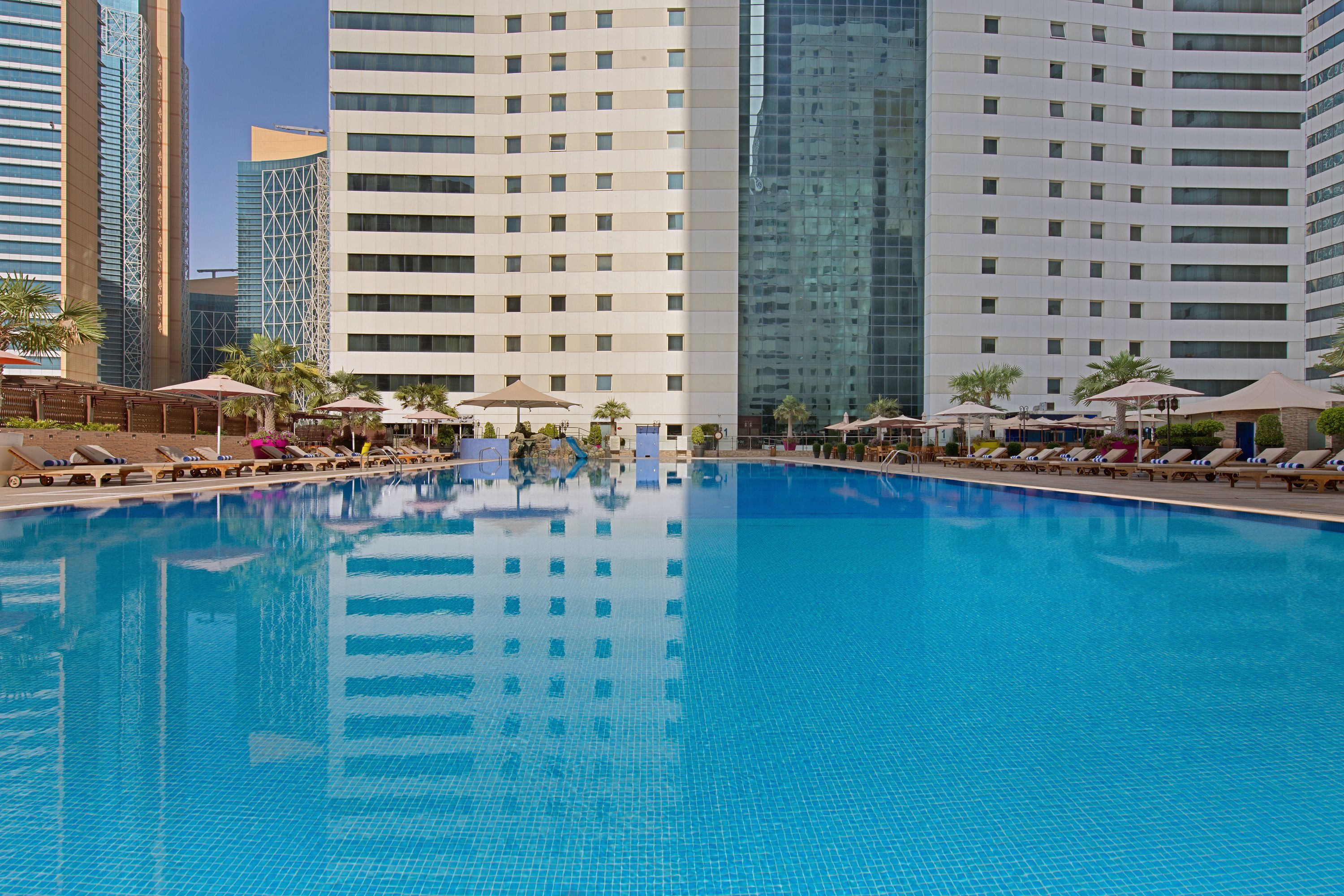 Una piscina al aire libre, sombrillas, sillones reclinables de piscina