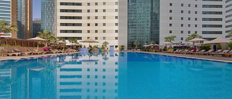 Una piscina con sillas de descanso y sombrillas, rodeada de edificios altos.