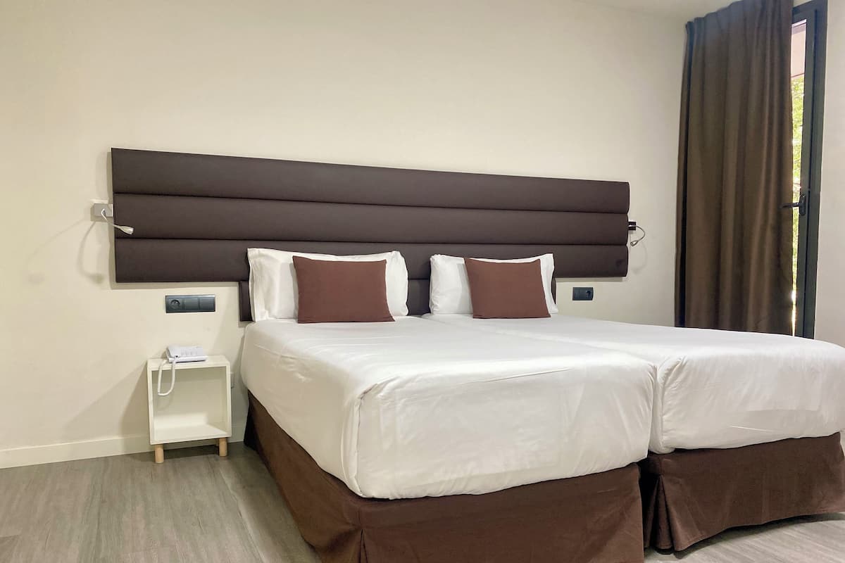 Habitación de hotel con una cama grande, una mesita de noche con teléfono y una ventana con cortinas.