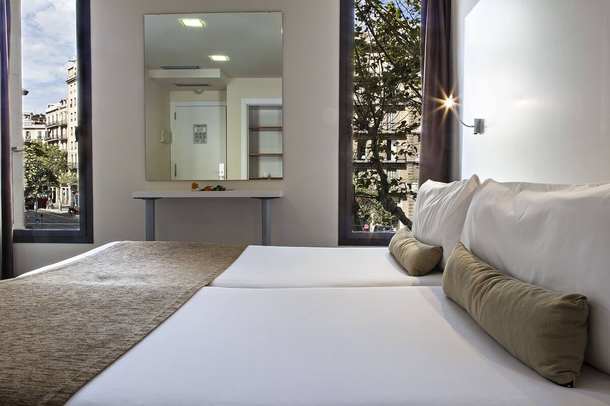 Un dormitorio moderno con una cama grande, un espejo y vistas de la ciudad a través de amplias ventanas.