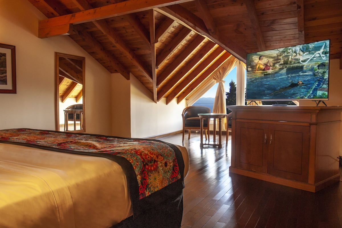 A bedroom with a large bed, wooden ceiling beams, a television, and a view of a swimming pool.