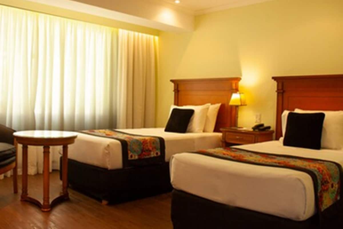 A hotel room with two beds, a small table, and a window with curtains.