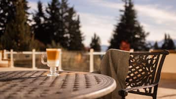 A round metal table with a glass of coffee and a grey shawl draped over a metal chair.