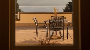Vista enmarcada de un patio con dos sillas y una mesa, con vista a un cuerpo de agua y montañas.