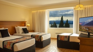 Habitación de hotel con dos camas, televisión y una ventana grande con vistas a la montaña.