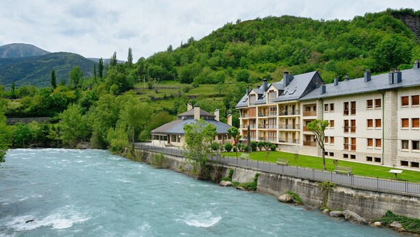 Un hotel con diversi piani, un fiume sullo sfondo e montagne all'orizzonte.