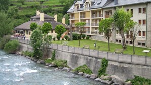 Un hotel con diversi piani, un fiume sullo sfondo e un paesaggio collinare in lontananza.