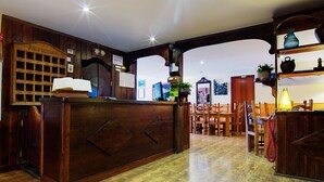 Una reception in legno con una sveglia e una bacheca. Si notano sedie e tavoli di legno sullo sfondo.