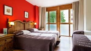 Una camera d'albergo con due letti, testiere in legno, una parete rossa e un'ampia finestra con tende.