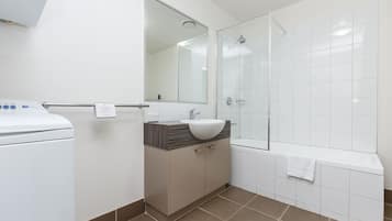 A modern bathroom with a white sink, a mirror, a shower, and a white toilet.