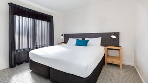 Hotellihuone, jossa on suuri sänky, yöpöytä, lamppu ja läpikuultavat verhot.