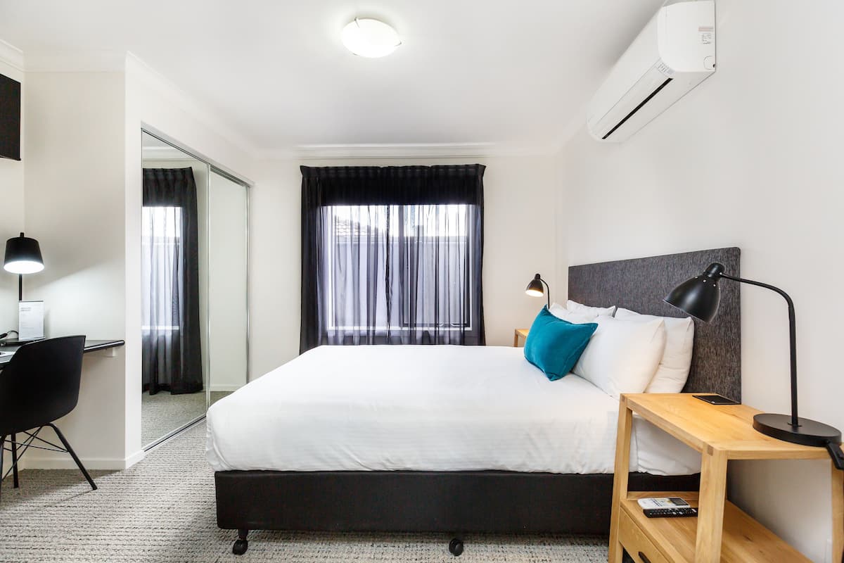 Una habitación de hotel con cama, mesita de noche, lámpara y escritorio con silla.