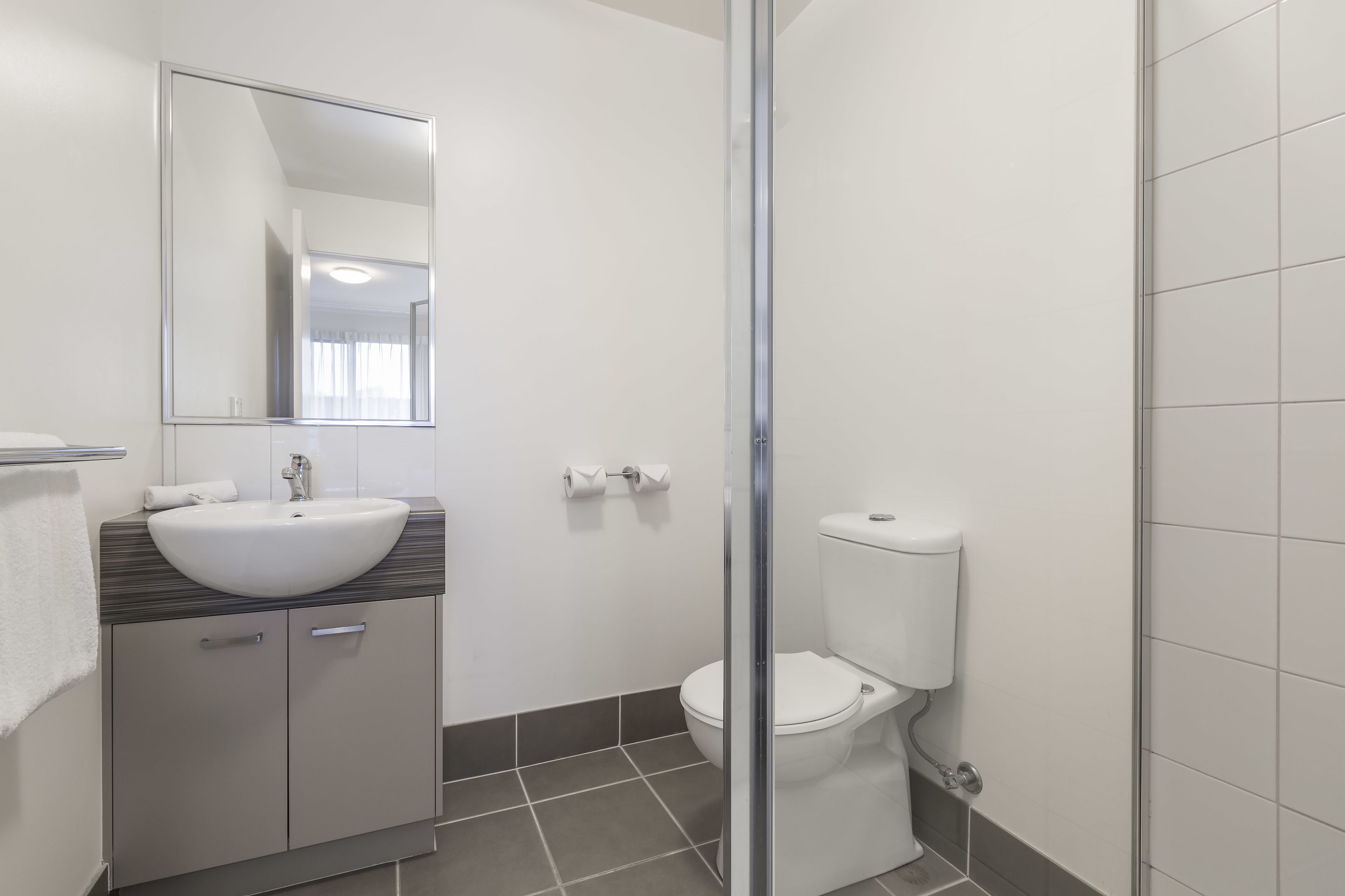 Ein modernes Badezimmer mit Waschbecken, Spiegel, Toilette und Duschbereich.