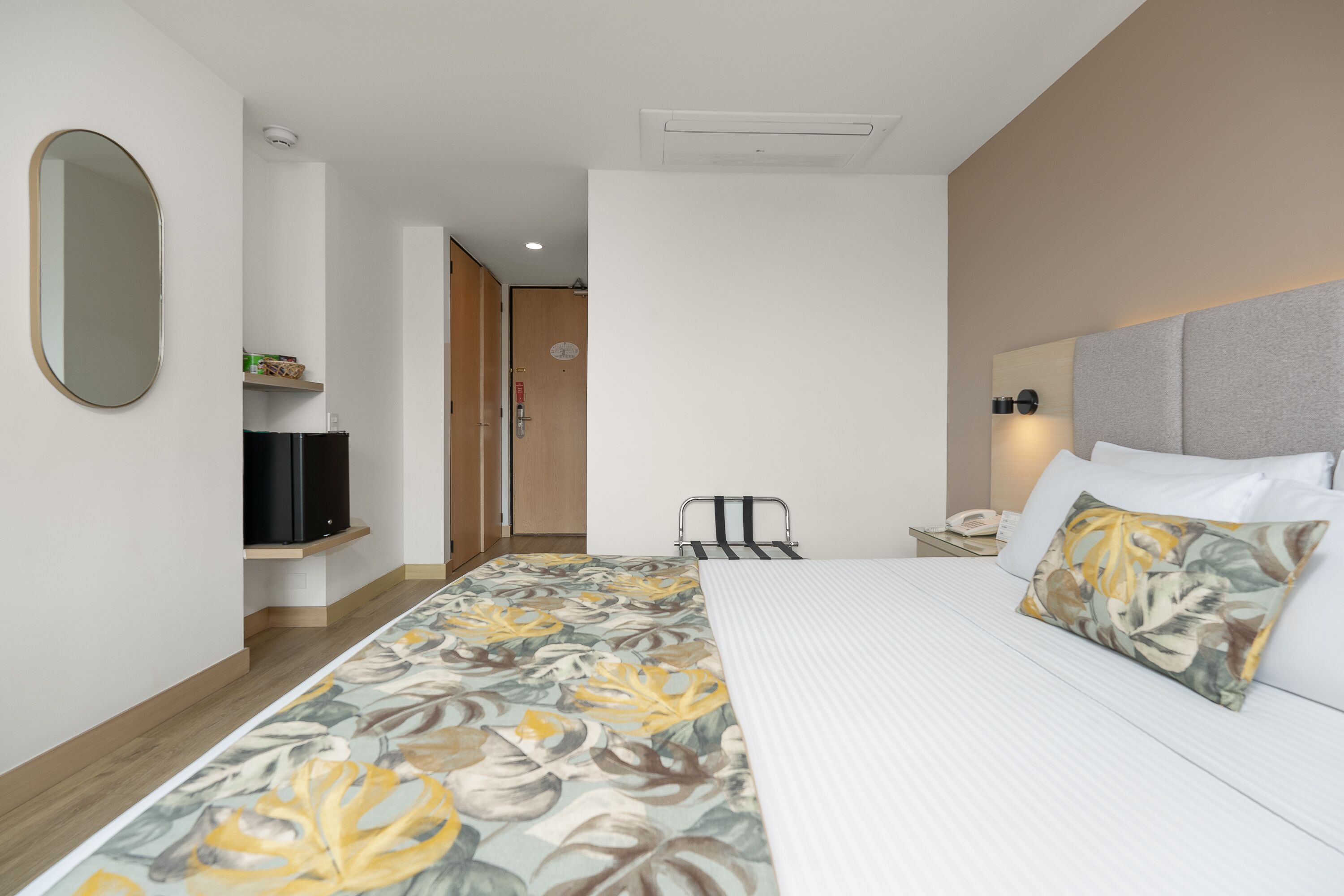 A hotel room with a bed, a TV on a shelf, a bedside table with a phone, and a headboard with a pillow.