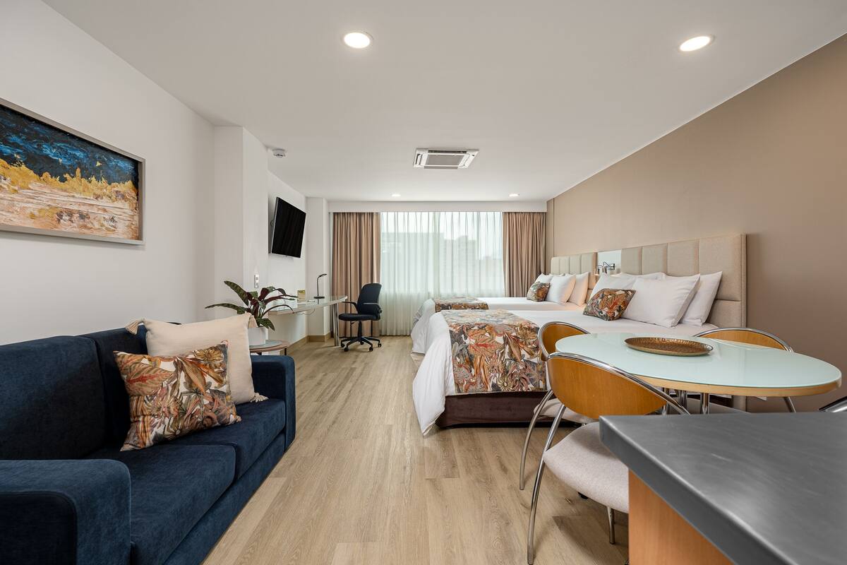 A hotel room with a bed, a sofa, a dining table, and a TV.