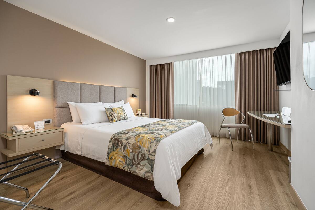 A modern hotel room with a large bed, bedside tables, a desk, and a chair.
