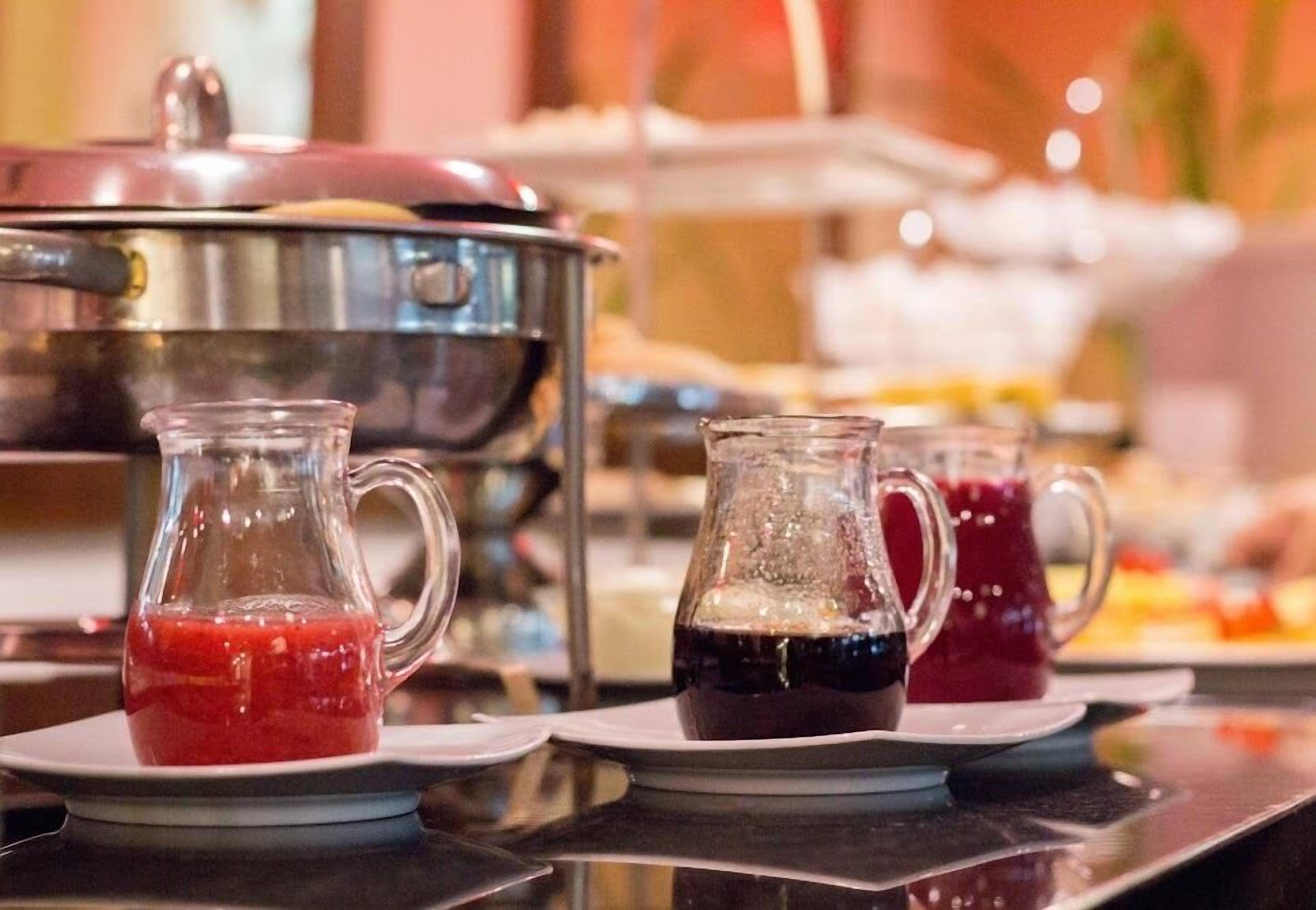 A buffet setup with various beverages in pitchers on plates, a large stainless steel pot, and a blurred background suggesting a dining area.