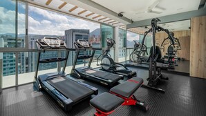 A gym with treadmills, an elliptical, and weight machines, with a city view through large windows. - Novelty Suites Hotel - Oviedo Mall (Medellín)