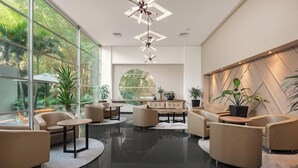 A modern lobby with a circular window, leather sofas, and a geometric light fixture. - Novelty Suites Hotel - Oviedo Mall (Medellín)