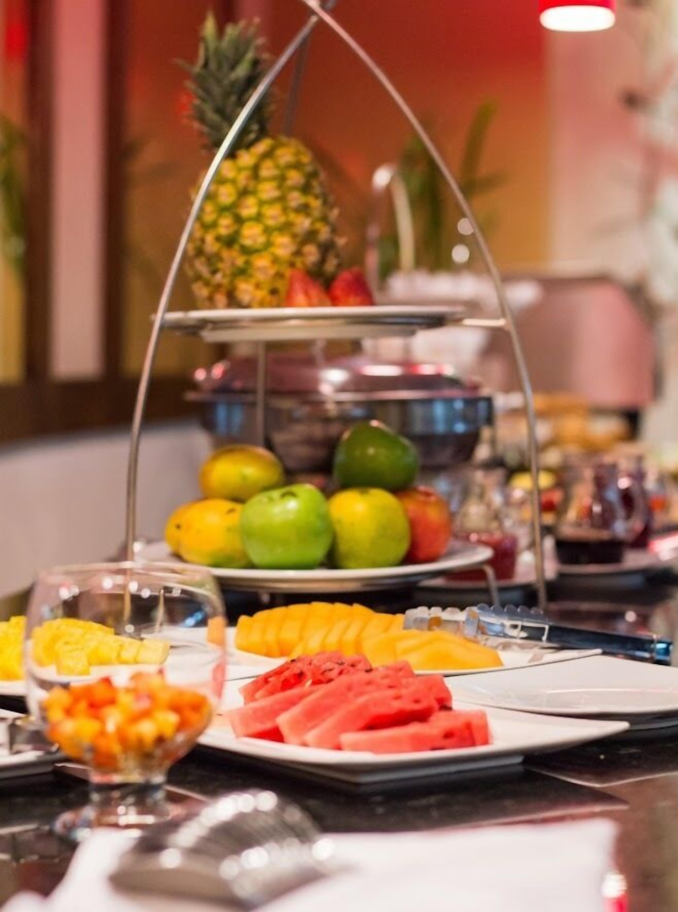 Un montaje tipo bufé con diversas frutas y una piña sobre un pedestal.