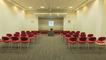 A conference room with rows of red chairs, a podium, and a projector screen.