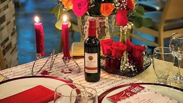 A table set for two with a candle, a bottle of wine, and a vase of red roses.