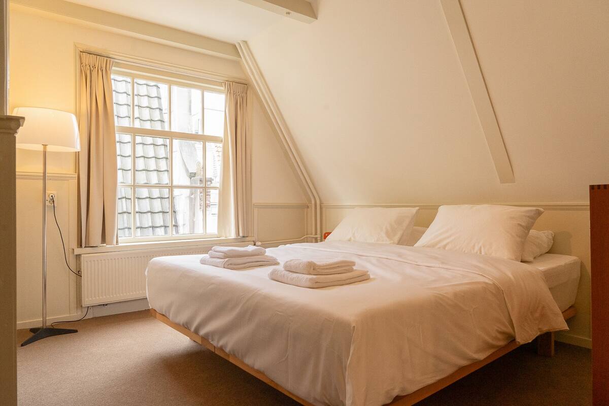 A bedroom with a large window, a radiator, and a bedside lamp.